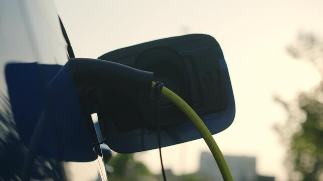 Female driver connects charging gun to electric car socket at ev charging station. Concept of promoting eco-friendly transportation solutions