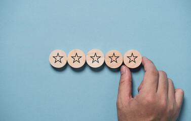 Hand input five stars on wooden block and blue background for the best customer satisfaction and...