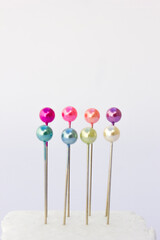 A close-up of small, silver straight pins neatly arranged on a white background. These pins are commonly used in sewing and crafting.