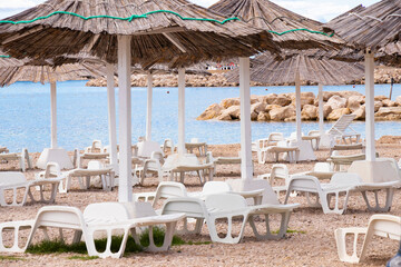 Straw beach umbrellas and sunbeds ready for rent in concessioned beachfront , with no people, on Croatian coast