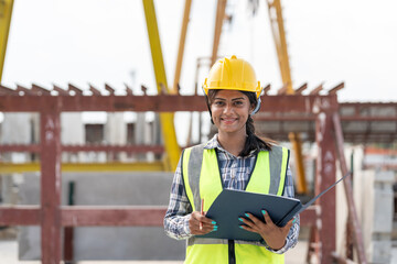 Asian woman engineer holding document smiling at construction site. Confident female Indian wearing...