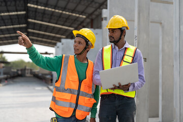 Asian male civil engineers wearing vest and helmet safety discussing foreman worker at construction site. Indian foreman with laptop working at factory making precast concrete wall.