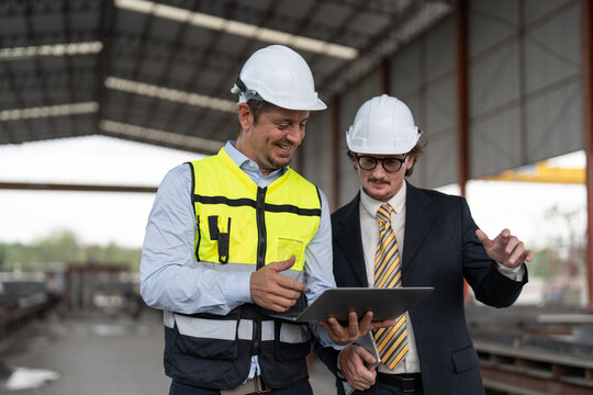 Businessman and male engineer walking and discussing the project making precast concrete wall at construction site.