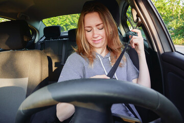 Young pretty female driver inside the auto puts on her seat belt.