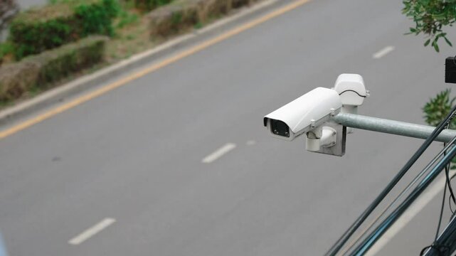 Close up of a surveillance enforcement camera monitor city traffic and speed control above the asphalt road. Defocused cars driving in the background. Road traffic safety copy space scene
