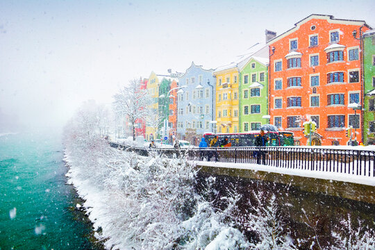 Snowy weather, colorful city houses, naked trees covered with snow and few people walk alongside the Inn river in Innsbruck, Tyrol (Tirol), western Austria, Europe