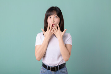 Smiling positive, asian young woman with surprised expression, hands on cheeks, isolated on green.