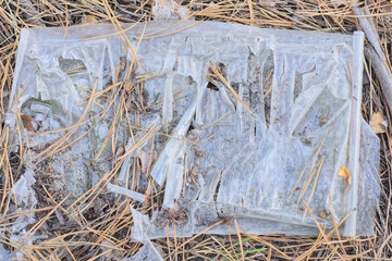garbage from one torn crumpled white plastic bag lies on gray earth in the street