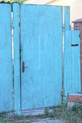 one closed metal blue green door on the wall of the fence on the rural summer street