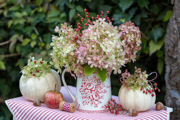 Blumenstrauß mit Rispenhortensien-Blüten und Hagebutten und weißen Kürbissen Baby Boo im Herbstgarten