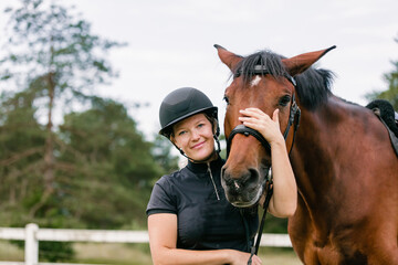 Woman with a black helmet stroking a beautiful chestnut horse head, close up shot. Human and animal...