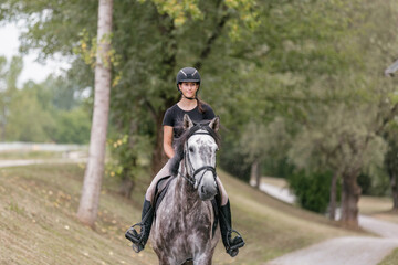 Female rider, horseback riding along the trail that leads between white wood fences and fields. Equestrian leisure activity concept.