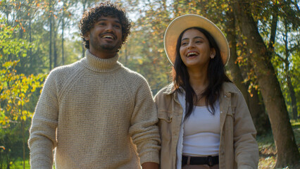 Carefree smiling family multiethnic couple in love Arabian Indian boyfriend male man guy pointing finger Hispanic girlfriend female woman lady walking in park hold hands laughing talking outdoors date