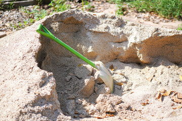 Green shovel placed on sand pile with sunlight at backyard patio with grass field for construction concept. DIY, Home improvement.
