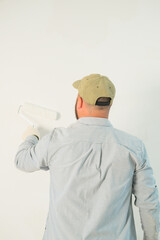 Back view of a man in construction gloves painting a wall with white paint using a roller. Renovation in a new house, preparing for a housewarming. Professional painter, handyman. Worker.