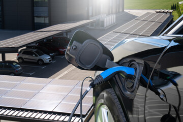 Naklejka premium Electric car is charging from a charging station that takes energy from solar panels. Close up.