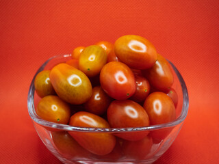 Cherry tomatoes in a glass bowl on a red background