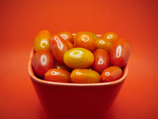 Cherry tomatoes in a glass bowl on a red background