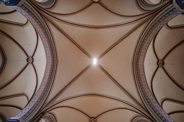 A close-up view of a church’s ornate vaulted ceiling with intricate arches and patterns, illuminated by soft light in the center..