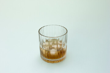 A clear glass with a textured exterior, partially filled with a brown liquid (possibly whiskey or tea). The liquid suggests it’s partially consumed or served in moderation.