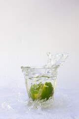 Water Splash Photography. A whole lime throw down in the small glass of water, creates a splash of water outside the glass.