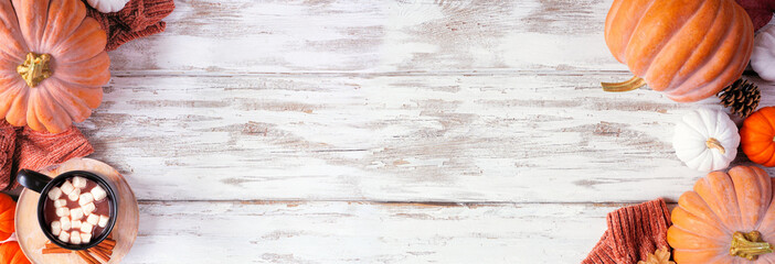 Cozy fall double border with pumpkins, sweaters and hot chocolate. Top view on a rustic white wood banner background.