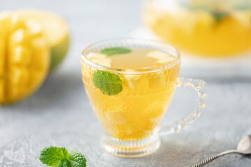 Fruit tea with mango and mint in a glass teacup on the table.