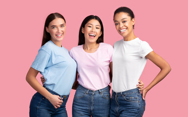 Obraz premium Three Joyful Diverse Women Hugging Standing On Pink Studio Background. Female Friendship.