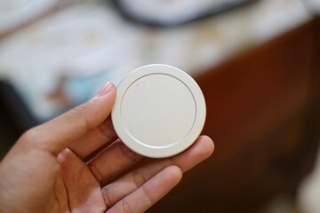 A hand holds a small silver metal disc, about quarter-sized, with a raised edge, likely a lens cap.