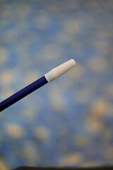 A close-up of a blue pen with a white tip, in focus, against a blurred blue and green liquid background.