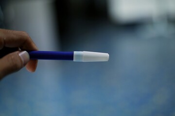 A close-up of a blue pen with a white tip, in focus, against a blurred blue and green liquid background.