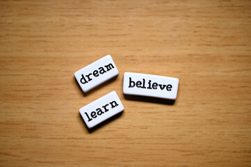 Motivation and self-improvement: blocks with the words 'dream', 'believe', and 'learn' on a wooden background, inspiring the journey towards personal and professional success.