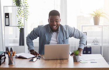 Pay Raise. Joyful african american worker looking at laptop screen with excitement, happy after...