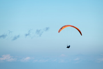 Paraglider in der Luft unter klarem, blauen Himmel mit orangenem Schirm