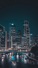 Naklejka premium Night cityscape with illuminated skyscrapers and a boat on a river, blue and black, modern city life. 