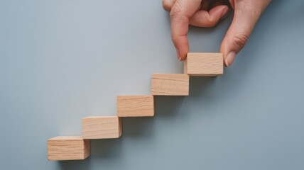 A close-up shot of a woman's hand arranging wooden blocks in a stack, forming a step staircase. The blocks are on a light blue background. The image is a business concept of growth, success