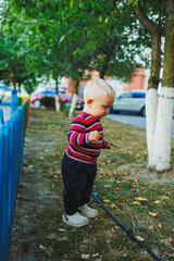 A fair-haired one-year-old boy in jeans and sneakers walks on the playground. The child develops and plays in the fresh air.