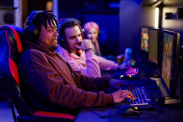 Interracial gamer with headset playing online video game in cybercafe.