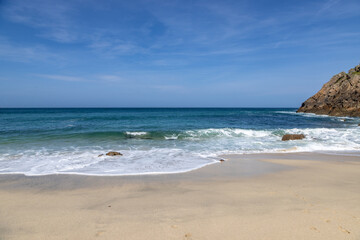 The idyllic sandy beach at Portheras Cove on the Cornish coast, with a blue sky overhead