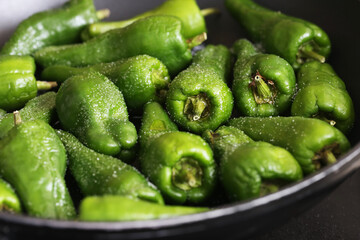 Pimientos de Padron background. Green peppers frying on a black pan. Cooking a Spanish delicacy, sprinkled with salt. Fresh vegetables sizzling in oil, traditional Spanish dish preparation.
