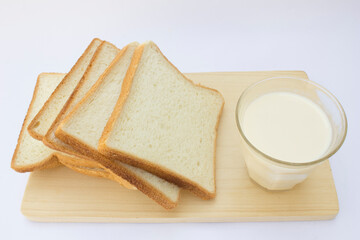 The glass of milk, transparent and inviting, contrasts with the soft texture of the fresh white bread slices. This simple yet classic pairing is ideal for breakfast or snack time.