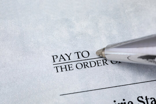 Writing check with pen. Banking, paying bills, and financial fraud concept