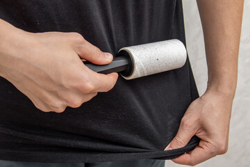 Man cleans black t-shirt with sticky roller. Cleaning clothes from dust, animal fur and hair. Dirty...