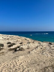 Rocky cliffside overlooking the deep blue sea under a clear sky in Ayia Napa, Cyprus. A peaceful coastal landscape with boats in the distance.
