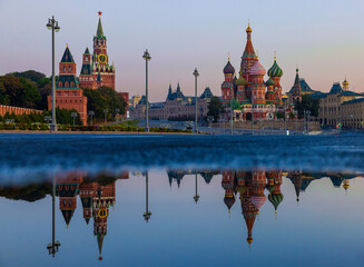 Fototapeta premium Twilight casts a beautiful glow on St. Basil's Cathedral and the Kremlin as they reflect in calm water in Red Square, showcasing Moscow's stunning architecture and historical significance at dusk.