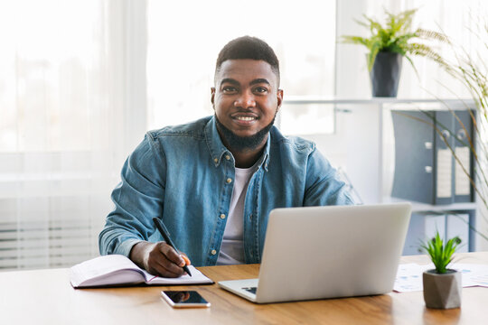 First day in office. Portrait of smiling african american trainee taking notes at new workplace, copy space