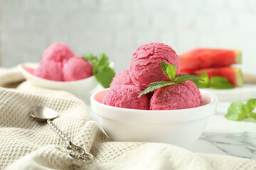 Scoops of tasty watermelon sorbet with mint in bowls and spoon on white marble table, closeup