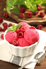 Delicious raspberry sorbet with fresh berries in bowl and spoon on wooden table