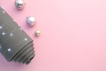 Yoga mat, baubles and Christmas lights on pink background, flat lay. Space for text