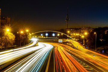 Traces of car lights at dusk driving along the Madrid ring road with the Piruli in the background